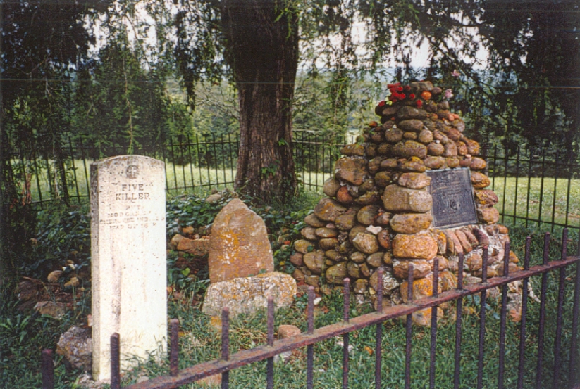 Nancy Ward's gravesite. Three gravestones are enclosed by an iron fence. Two are headstones but a large pile of rocks on the far right marks grave three.